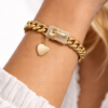 Chunky gold chain bracelet with heart charm worn on woman’s wrist.