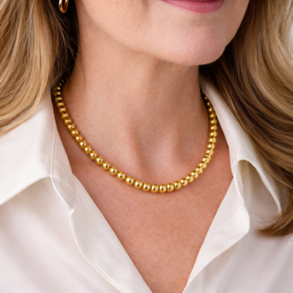 Woman wearing gold stainless steel bead necklace with white blouse close-up
