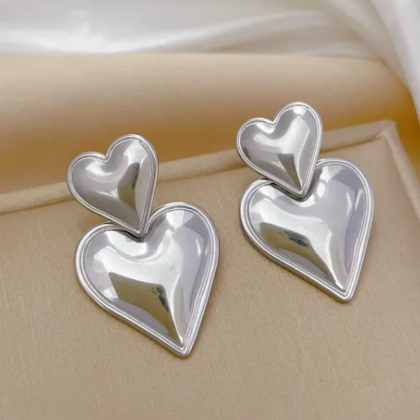 Close-up of silver double heart statement earrings on beige background