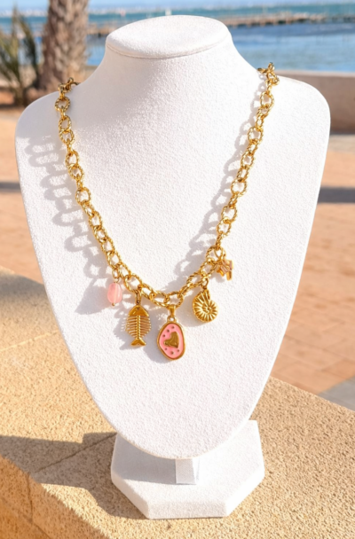 Gouden stainless steel schakelketting met bedels waaronder een roze hart, vis en schelp op zwarte achtergrond