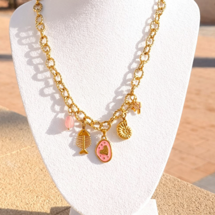 Gouden stainless steel schakelketting met bedels waaronder een roze hart, vis en schelp op zwarte achtergrond