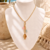The ocean whisper necklace Gold toned stainless steel necklace with fish charm and pastel pink and blue details displayed in an Ibiza inspired beach setting