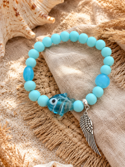 Ocean Angel Bracelet Soft blue elastic bracelet with acrylic beads, glass fish charm and silver wing pendant on a beachy boho background