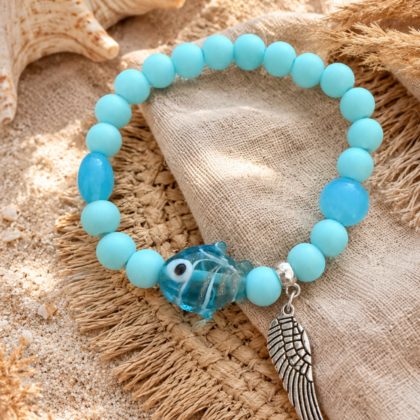 Ocean Angel Bracelet Soft blue elastic bracelet with acrylic beads, glass fish charm and silver wing pendant on a beachy boho background