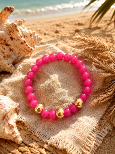 Pink Paradise Bracelet Bright pink elastic bracelet with acrylic beads and gold accents styled on a beachy summer background