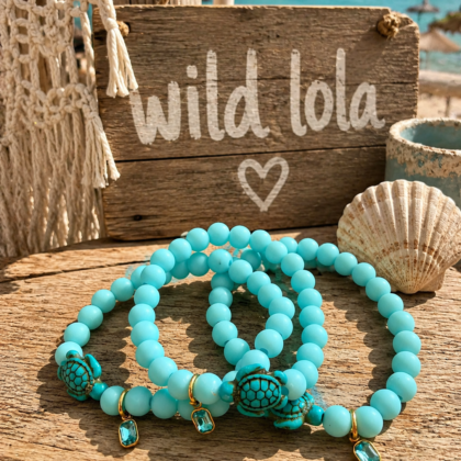 Wild Lola – Sea Turtle Bracelet Handmade aqua elastic bracelet with sea turtle charm and crystal detail displayed on a beach-inspired boho background.