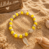 Wild Lola Sunshine Turtle Bracelet Yellow acrylic bead bracelet with beach-inspired charm and turtle detail displayed on sandy beach background with Wild Lola sign.