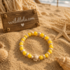 ChatGPT Image 31 mei 2026, 18_46_47 Yellow acrylic bead bracelet with beach-inspired charm and turtle detail displayed on sandy beach background with Wild Lola sign.