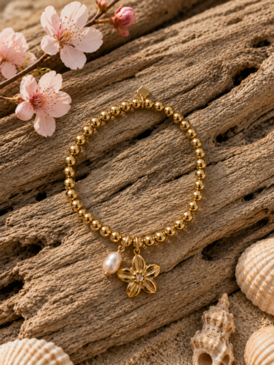 Pearl Bloom Bracelet β Gold Stainless Steel Gold stainless steel beaded bracelet with freshwater pearl charm and flower pendant displayed on driftwood with cherry blossom accents.