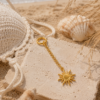 Wild Lola Bikini Charm Sunbeam Gold Gold sun bikini charm with delicate chain displayed on a sandy beach in a boho-inspired summer setting.