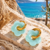 Wild Lola Mint Bloom Earrings wearing gold-tone stainless steel hoop earrings with mint-green flower charms in a boho beach setting.