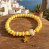 Ibiza Sunshine Turtle Bracelet Yellow Ibiza bracelet with turtle bead and gold flower charm displayed in a beach-inspired boho setting.